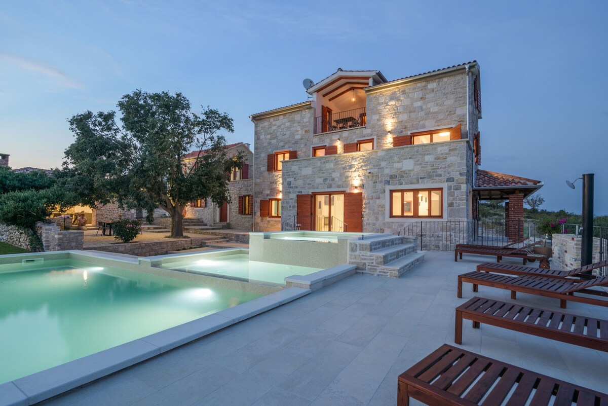 Authentic Stone Villa illuminated at dusk beside the heated pool